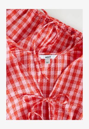 Blouse à carreaux rouge et rose avec un décolleté froncé et un détail à nouer. Fabriquée en tissu léger, elle comporte une étiquette "NEXT" à l'intérieur.