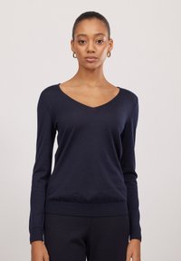 Navy V-Ausschnittpullover mit langen Ärmeln, tailliert an der Taille und den Bündchen, aus einem glatten, weichen Material, das ein einfaches, klassisches Design zeigt.