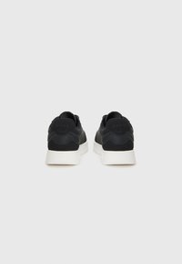 Black sneakers with a smooth upper, textured accents, and a white rubber sole. Features logo detailing and a low profile design.