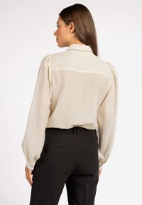 Cream-colored blouse with puffed long sleeves, textured fabric, and a buttoned collar, paired with black tailored pants.