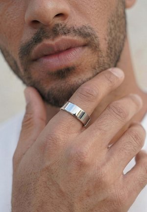 Man with stubble touching his chin, wearing a wide, polished silver ring on his middle finger.