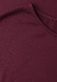 Gros plan sur un tissu violet foncé lisse avec des coutures visibles près d'une couture courbe, montrant les détails de la texture et du tissage.