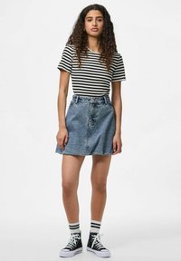 T-shirt rayé noir et blanc, jupe en denim bleu clair taille haute, baskets noires avec semelles blanches et chaussettes rayées.
