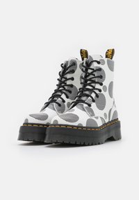 Białe botki za kostkę z czarno-białym paskowanym wzorem w groszki, czarnymi sznurówkami, żółtymi akcentami w ściegach i grubą czarną gumową podeszwą.