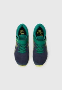 Baskets de sport bleu marine et vert avec tige en maille, bande réglable, lacets verts et accents jaunes vifs sur la semelle et le logo.