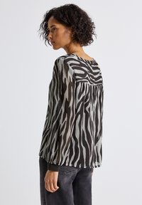 Blusa trasparente con un motivo zebra in nero e grigio, maniche lunghe e vestibilità rilassata. Dettaglio dello sprone sulla parte posteriore visibile sopra la sezione arricciata.