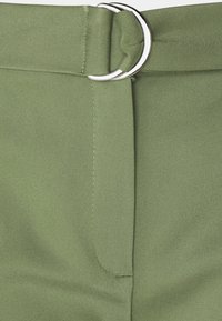 Close-up of light green fabric pants with a matching belt threaded through a silver double-ring buckle.