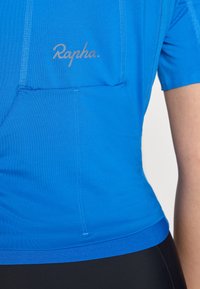 Blå cykeltröja med korta ärmar, med en texturerad tyg och en liten bröstficka. "Rapha."-logotypen är tryckt i grått.