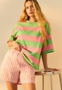 Camiseta oversize de rayas verdes y rosas combinada con pantalones cortos de rayas rosas y blancas. Tejido suave, corte relajado y mangas enrolladas.