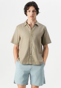 Chemise à manches courtes kaki texturée avec un design à boutons, associée à un short en denim bleu clair. Dispose d'un col standard et de poches latérales.