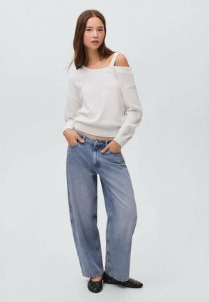 Weißer, schulterfreier Strickpullover mit geripptem Saum, kombiniert mit hoch taillierten, weit geschnittenen hellblauen Jeans und schwarzen Slippern mit Nieten.