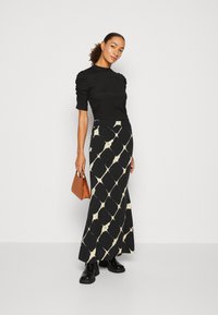 Black fitted top with puffed short sleeves paired with a long black skirt featuring a cream geometric pattern. Brown handbag and black boots.