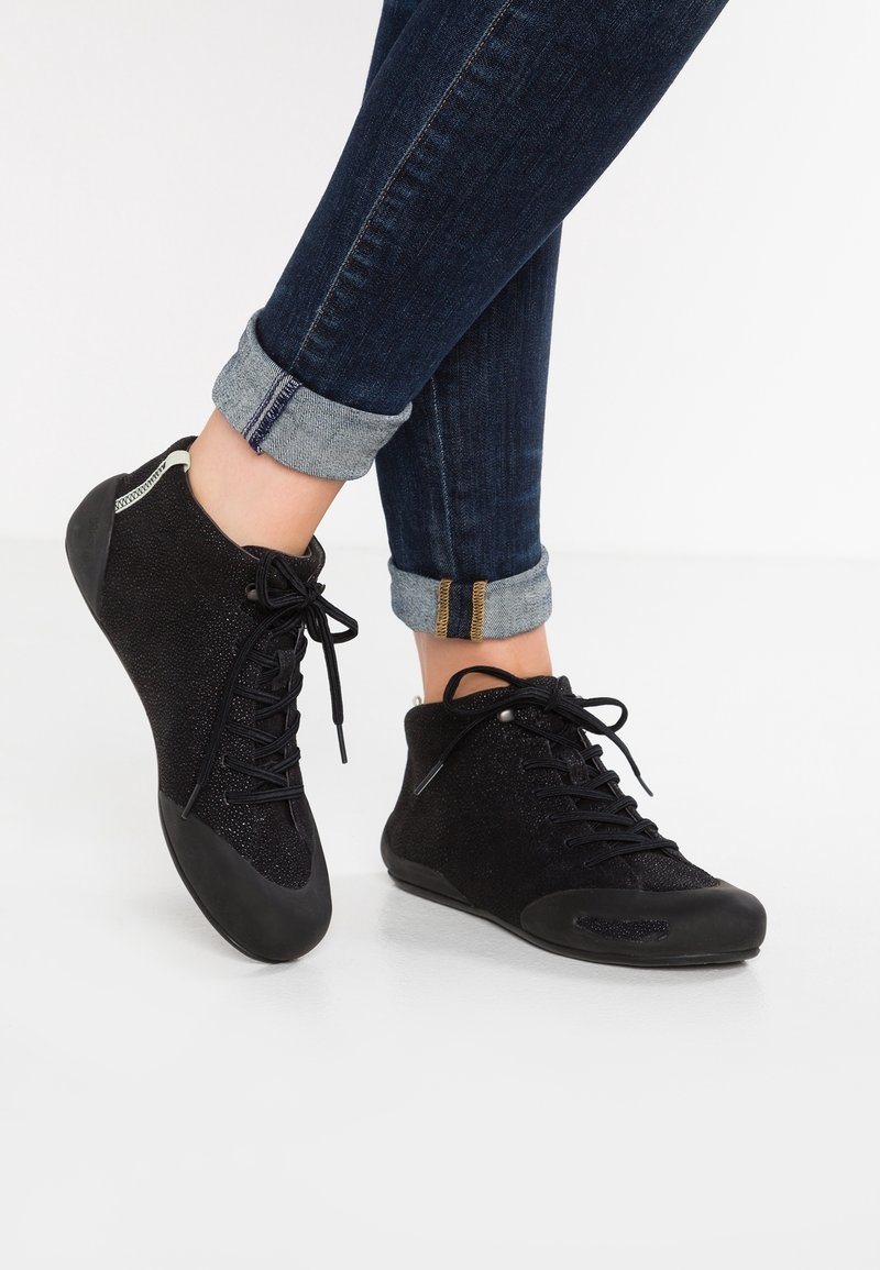 Black high-top shoes with a textured fabric upper, laced front, and rubber soles. The design includes a shiny finish and contrasting accents.