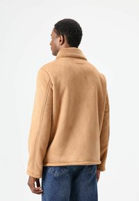 Bruine fleece jas met een zachte, getextureerde kraag. Heeft een klassiek ontwerp, rechte snit en zichtbare naden. Draagt over spijkerbroeken.