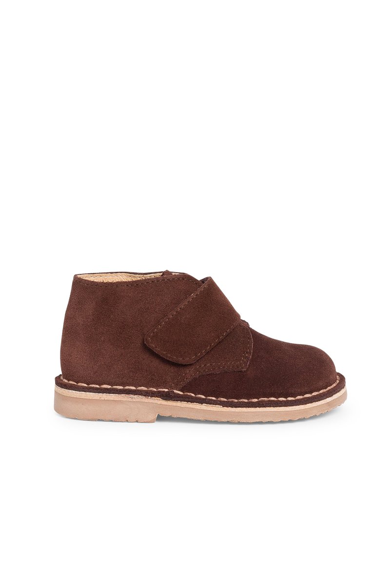 Botas de tobillo de ante marrón con punta redondeada, que cuentan con una correa de gancho y bucle y una suela de goma de color claro. Textura suave, diseño sencillo.