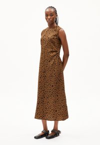 Brown sleeveless dress with black spotted pattern, midi length, soft fabric, side seams, worn with black shoes featuring accents.