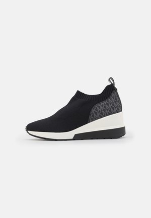 Sort slip-on sneaker med strikket overdel, hvid kileformet sål og mønstret hælpanel med mærkevarelogo.
