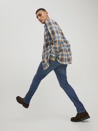 Men's plaid flannel shirt in blue, brown, and cream, paired with blue jeans and brown ankle boots. Features a casual fit and long sleeves.