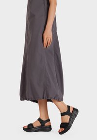 Infradito neri regolabili con suola spessa, caratterizzate da due cinturini e una tomaia in tessuto texture. Abbinati a un vestito maxi grigio fluente.