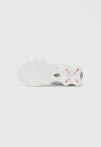 Sola de um tênis atlético branco com borracha texturizada apresentando padrões circulares e em onda, e detalhes em vermelho perto do calcanhar.