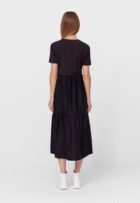 Czarna sukienka z krótkim rękawem i falbanistą spódnicą. Wykonana z miękkiego materiału, ma luźny krój i sięga do połowy łydki.