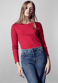 Rode langärmige top met een ronde halslijn, gecombineerd met high-waisted blauwe jeans met een klassieke vijf-pocket ontwerp en subtiele vervaging.