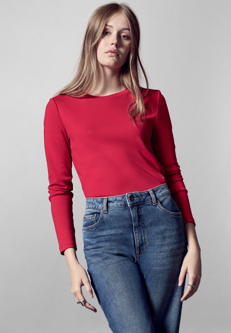 Rode langärmige top met een ronde halslijn, gecombineerd met high-waisted blauwe jeans met een klassieke vijf-pocket ontwerp en subtiele vervaging.