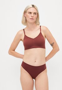 Barna vezeték nélküli bralette csipke díszítéssel, hozzá illő, magas derekú bugyival párosítva. Sima anyag, minimalista dizájn és egyszerű pántok.