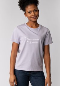 Lavendel T-shirt met korte mouwen, gemaakt van zachte stof, met de witte tekst "Was muss, das muss" op de voorkant, gecombineerd met donkere jeans.