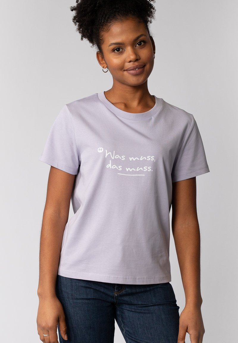 Lavendel T-shirt met korte mouwen, gemaakt van zachte stof, met de witte tekst "Was muss, das muss" op de voorkant, gecombineerd met donkere jeans.