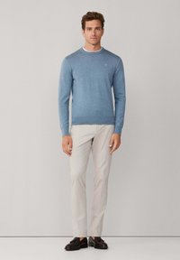 Lichtblauwe gebreide trui met een ronde hals, lange mouwen en geribbelde zoom, gecombineerd met beige broek en donkere schoenen. Gladde textuur.