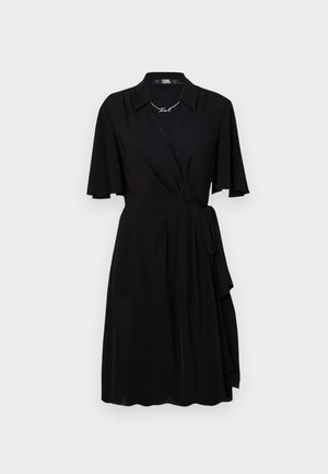 Musta neulemekko, jossa on kaulus, lyhyet hihat ja vyö vyötäröllä. Valmistettu sileästä kankaasta, jossa on virtaviivainen muotoilu ja kaareva helma.