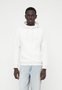 Sweatshirt à capuche gris clair, en tissu doux avec une poche avant, arborant un logo en relief subtil et des poignets et un ourlet côtelés.