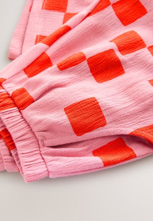 Tissu rose avec une surface texturée présentant des carrés rouges audacieux de tailles variées, détail de taille élastique froncée, et tombé souple.