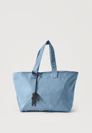 Sac fourre-tout en tissu bleu clair avec deux anses et un porte-clés noir en forme de lapin accroché à l'une des anses.