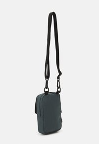 Saco retangular em teal escuro com uma textura de tecido suave, alça preta ajustável e compartimento com fecho. Design minimalista sem hardware em destaque.