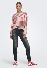 Camisa de rayas de manga larga en crema y rojo, combinada con jeans ajustados oscuros con desgarros, y zapatillas rojas y blancas de diseño deportivo.