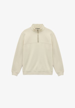 Pull à manches longues couleur crème avec col demi-zip et poignets côtelés, posé à plat sur un fond blanc.