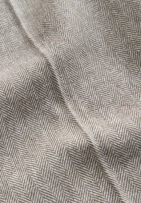 Primer plano de tela tejida con patrón espiga en beige y blanco con pliegues suaves y superficie texturizada.