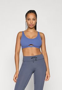 Μπλε αθλητικό bralette με λεπτομέρεια cutout, φαρδιές τιράντες, συνδυασμένο με γκρι κολάν ψηλής μέσης που διαθέτουν κορδόνι και ραφές.