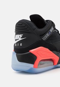 Black Nike Air Max sneaker with red accent, translucent sole air cushion, and white Nike logo on heel, viewed from rear side.