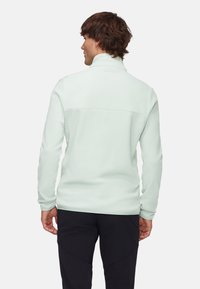 Light mint green fleece jacket with a high collar and seam detail on the back, paired with black pants. Soft texture, long sleeves.