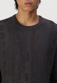 Ciemnoszary dzianinowy sweter z teksturowanymi wzorami i otwartymi splotami, z prążkowanym okrągłym dekoltem i złożonymi detalami na tkaninie.