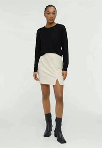 Black long-sleeve top and a light beige mini skirt with a side slit, paired with knee-high black boots. Smooth texture, fitted design.