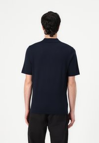 Polo bleu marine à manches courtes et col classique, fabriqué en matériau doux, avec une texture unie sans motifs.