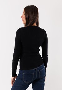 Top a maniche lunghe nero a coste con un design attillato, abbinato a jeans blu scuro con tasche posteriori e una leggera elasticità.