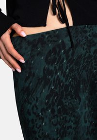 Falda verde oscura con un patrón de estampado de leopardo negro, hecha de una tela suave. Presenta un diseño ajustado y un cierre con cordón en la cintura.