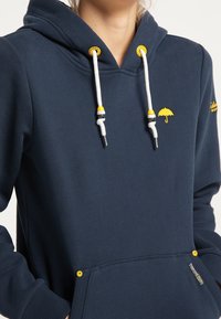 Felpa blu navy con tasca a marsupio, accenti gialli sui lacci e logo di un ombrello, realizzata in tessuto morbido con una superficie liscia.
