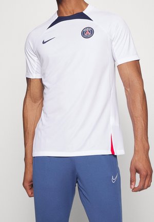 Mand iført hvid Paris Saint-Germain fodboldtrøje med marineblå og røde detaljer og blå Nike atletikbukser.