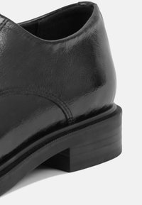 Scarpa in pelle nera con finitura liscia, punta rotonda e tacco basso impilato. Dettagli cuciti lungo la parte superiore per un tocco in più.